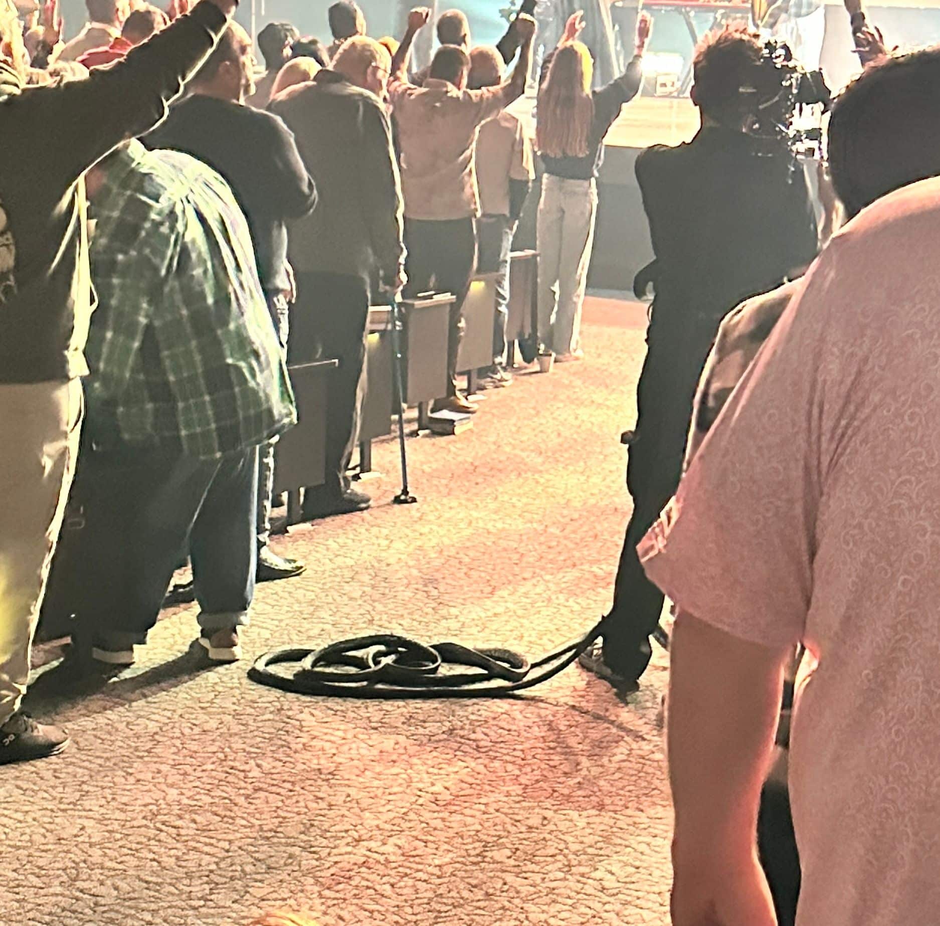 Worshippers with hands raised during a service, with a coiled cable lying on the aisle carpet.